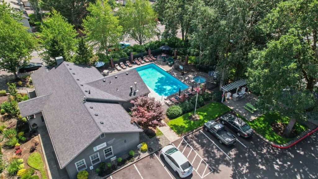 aerial view of outdoor swimming pool and hot tub next to leasing office, with grilling and picnic area nearby