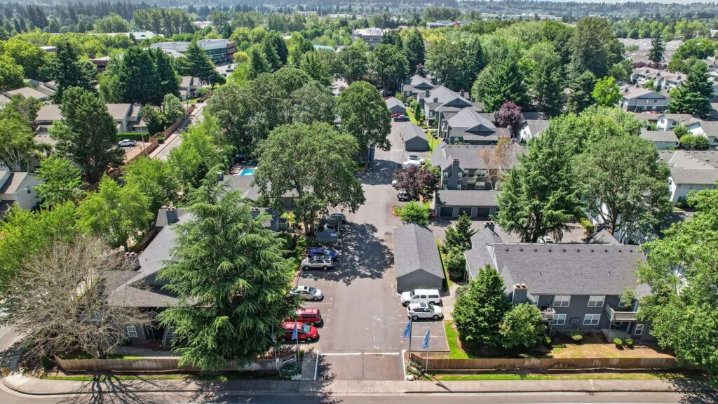 exterior aerial view of apartment complex entrance with covered and open parking and lush foliage